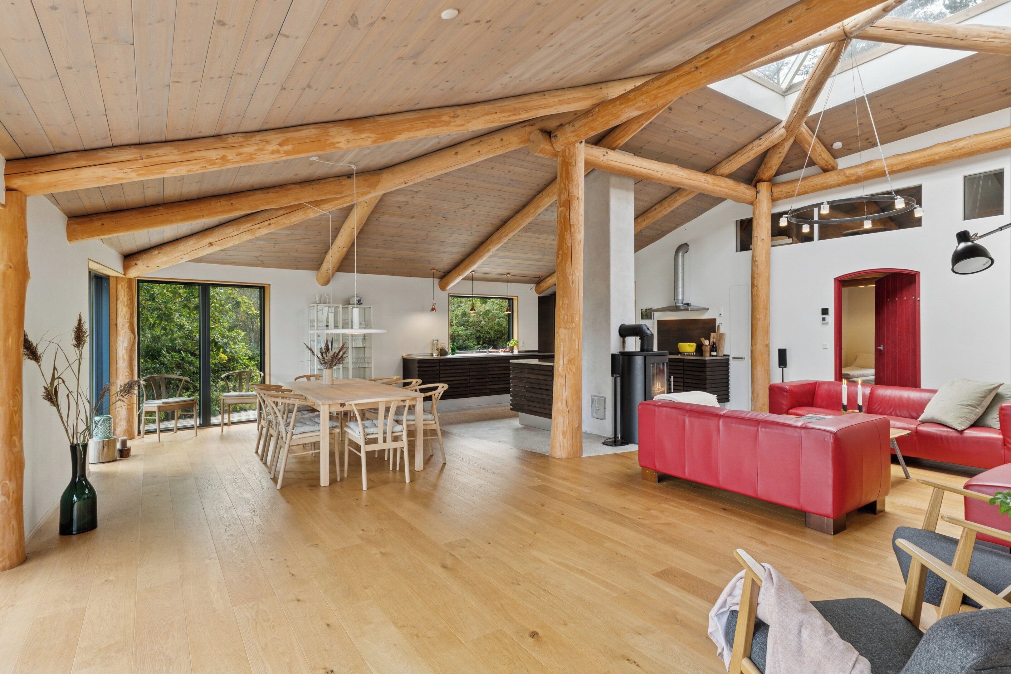 A spacious interior with wooden beams, a dining area, a red sofa, and a kitchen.