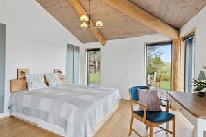 Une chambre avec un grand lit, des poutres apparentes en bois au plafond, un bureau et une chaise.