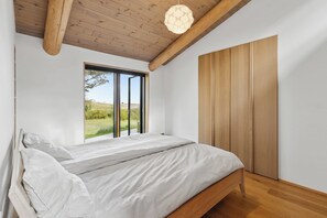 Ein Schlafzimmer mit Bett, Fenster, Holzbalken an der Decke und einem Holzschrank.