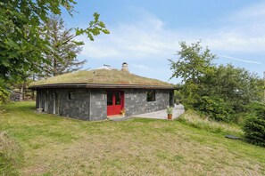 Ein kleines Steinhaus mit roter Tür, einem Rasen und einem Strohdach.
