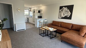 Ein modernes Wohnzimmer mit einem braunen Sofa, einem kleinen Tisch und einer Küche im Hintergrund.