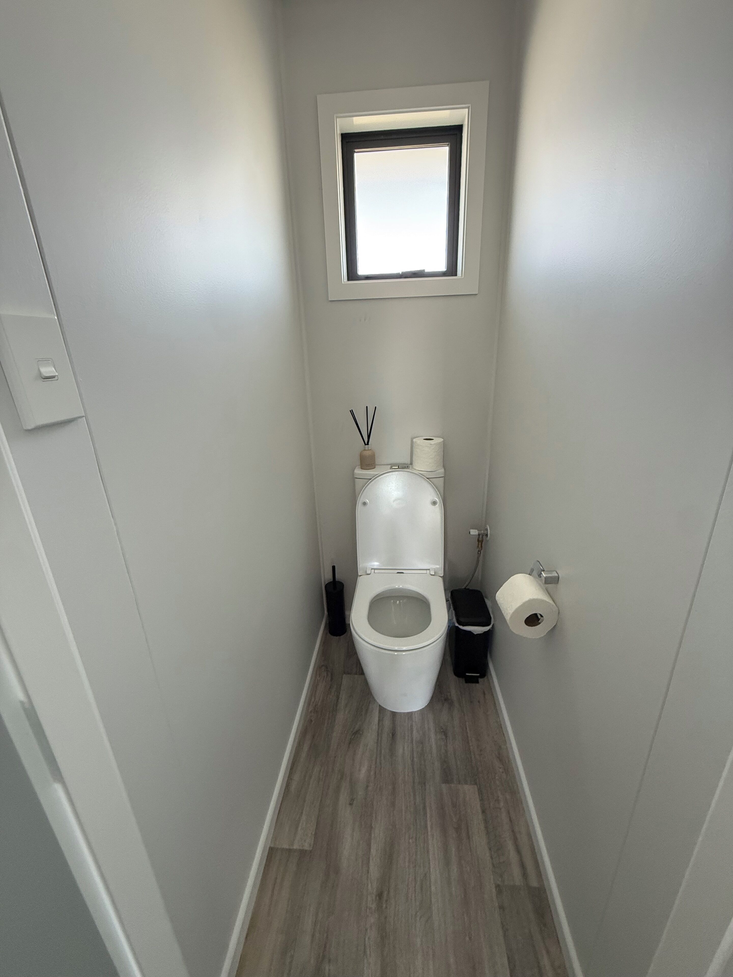 Un baño reducido con inodoro, una ventana pequeña y un cesto de basura.