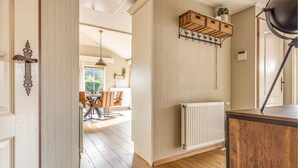 Un corridoio con pavimento in legno, termosifone bianco, mensola a cestino in vimini e una porta con maniglia decorata.
