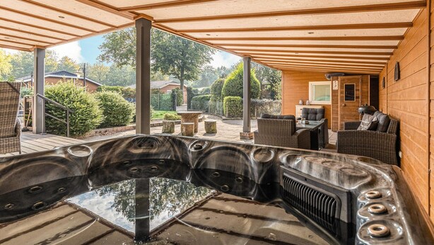 Una vasca idromassaggio con una pergola in legno sopra, area salotto esterna e vista su una zona residenziale.