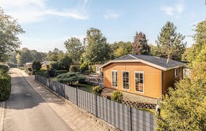 A wooden cabin with a sloped roof, surrounded by a fenced yard with various shrubs and trees. - 3 bedroom stunning home in Erm (Erm)