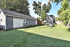 A residential backyard with a garage, a wooden deck, and a dining area with outdoor furniture.