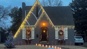 A house with a triangular roof, decorated with string lights and wreaths.