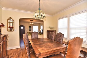 A dining room with a wooden table and patterned chairs, a chandelier, and a mirror on the wall.