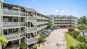 A multi-story hotel with a central courtyard, outdoor parking, and a pool area. - North Myrtle Beach 2BR Condo – Pool, Fire Pit and Pet-Friendly (North Myrtle Beach)