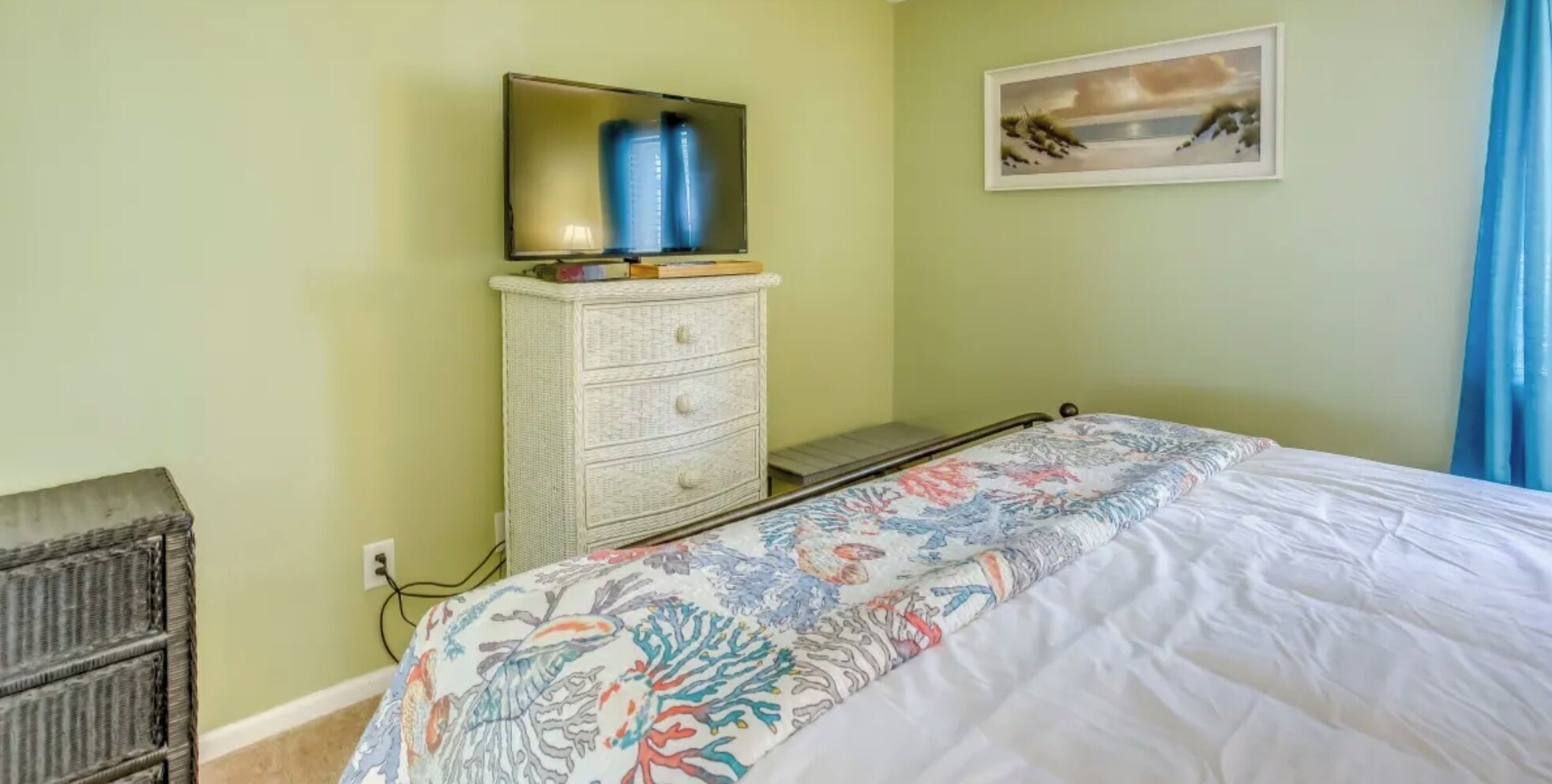 Een slaapkamer met een bed, een dressoir, een televisie bovenop het dressoir en een schilderij aan de muur.