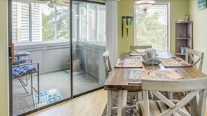 A dining area with a wooden table, chairs, and a glass partition. - North Myrtle Beach 2BR Condo – Pool, Fire Pit and Pet-Friendly (North Myrtle Beach)
