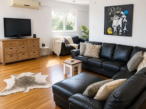 A living room with a black leather sofa, a wooden cabinet, a television, and a painting on the wall.