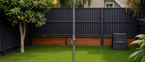 A backyard with a clothesline, a tree, a wooden fence, and a trash bin.