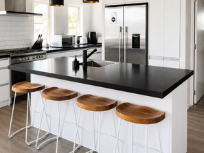 Eine moderne Küche mit einer Kochinsel, Barhocker, Edelstahlgeräten und einer weißen Spritzschutzwand.
