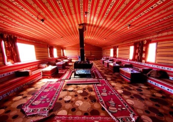 A traditional room with a central fireplace, patterned rugs, and wooden benches along the walls. - Wadi Rum Moon (Wadi Rum)