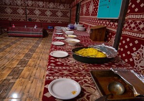 A long dining table with various dishes and a large bowl of food, set in a room with patterned walls and wooden flooring. - Wadi Rum Moon (Wadi Rum)