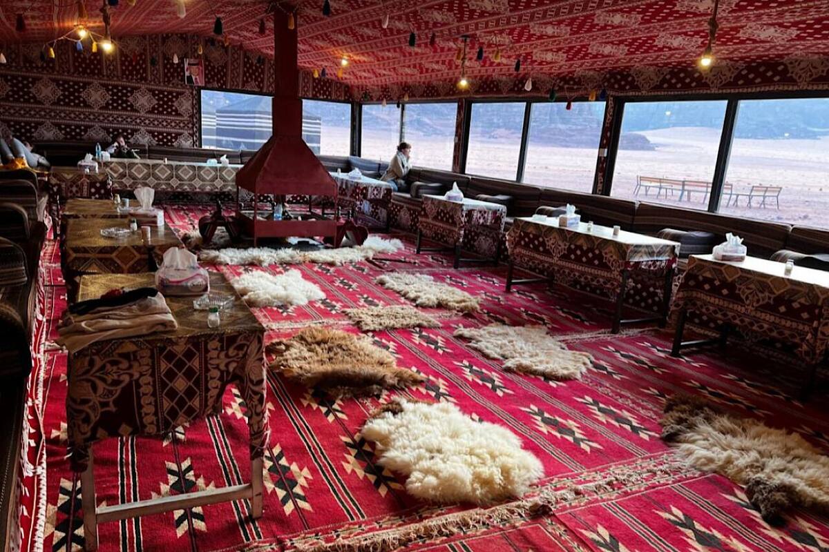 A restaurant with a patterned red carpet, wooden tables, and benches.