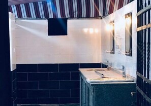A bathroom with a tiled floor, a sink with a mirror, and a wall-mounted light fixture. - Wadi Rum Moon (Wadi Rum)