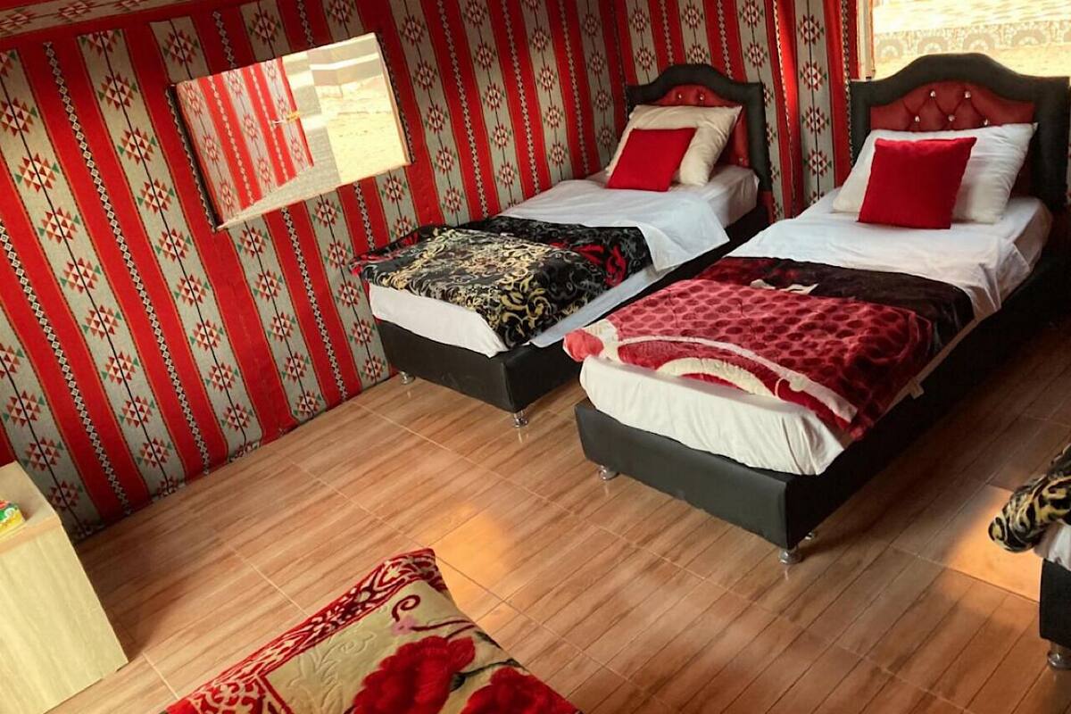 A room with two beds, a wooden floor, and patterned wallpaper.