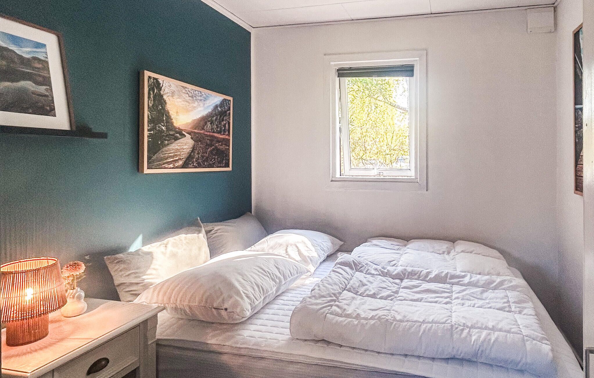 A bedroom with a bed, a nightstand, a lamp, a window, and a painting on the wall.
