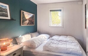 A bedroom with a bed, a nightstand, a lamp, a window, and a painting on the wall.
