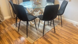 A dining area with a glass table surrounded by four black chairs, a small plant, and a white wall with a picture frame. - Charming 3-bedroom house in Sittingbourne for contractors, family & Tourists!! (Sittingbourne)