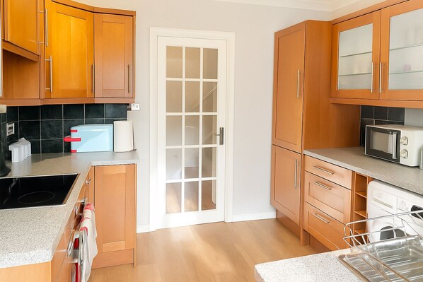 A kitchen with wooden cabinets, a microwave, a toaster, and a sink. - Charming 3-bedroom house in Sittingbourne for contractors, family & Tourists!! (Sittingbourne)