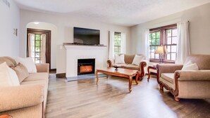 A living room with a fireplace, two sofas, a coffee table, and a TV mounted above the fireplace. - Hot tub, 4bd Family Home - Bertrand Cottage (Manhattan)