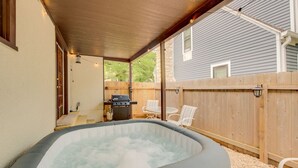 A hot tub in a covered outdoor area with a wooden deck, a barbecue grill, and white chairs. - Hot tub, 4bd Family Home - Bertrand Cottage (Manhattan)