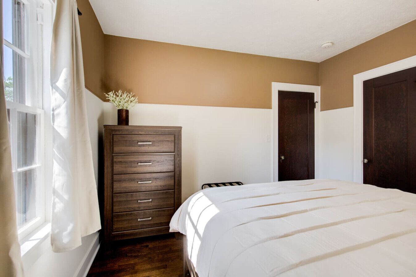 A bedroom with a bed, a dresser, a door, and a window with curtains.