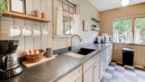 A kitchen with wooden cabinets, a black countertop, a coffee maker, and hanging mugs. - Hot tub, 4bd Family Home - Bertrand Cottage (Manhattan)