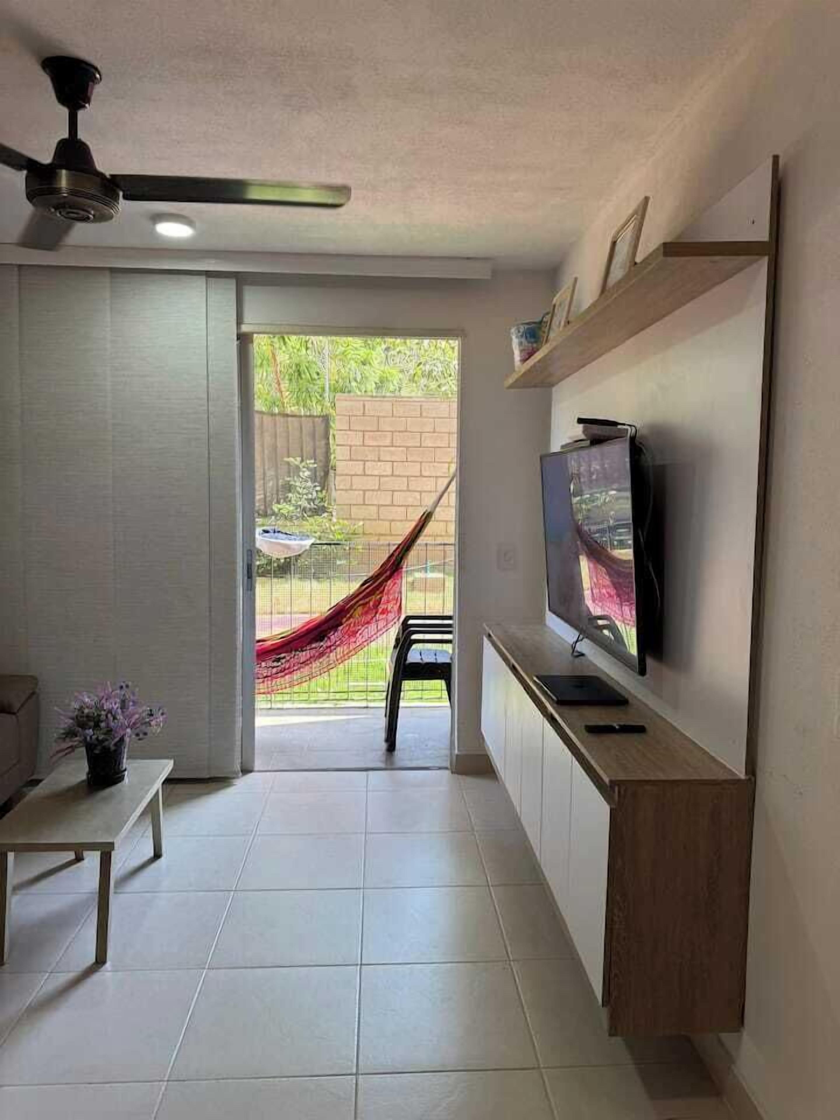 Un salon moderne avec un téléviseur à écran plat fixé à un meuble en bois, un ventilateur de plafond et un hamac à l’arrière-plan.