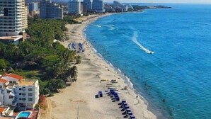 A beach with rows of sun loungers and a few palm trees. - Santa Marta - pozos colorados playa (Santa Marta)