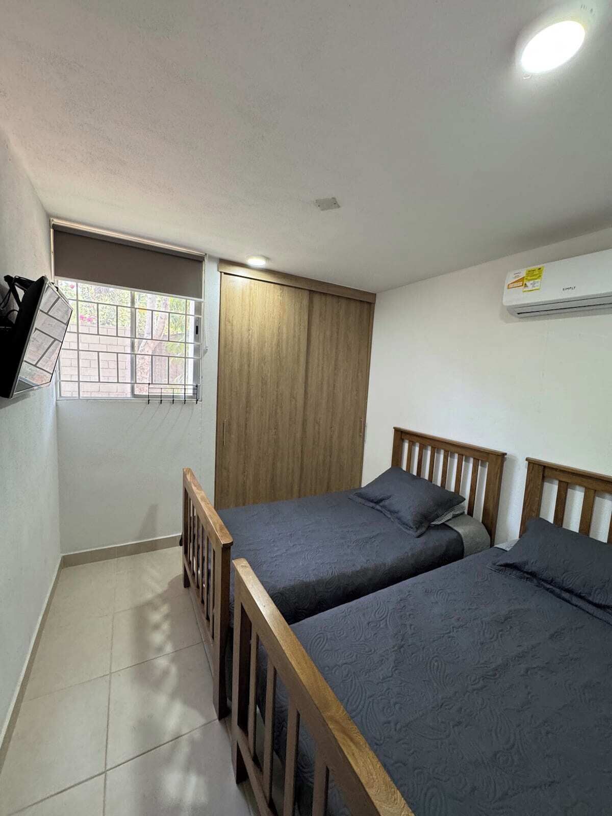 Une petite chambre propre, avec deux lits simples, une fenêtre donnant sur un paysage agréable, un luminaire au plafond et un appareil de climatisation.