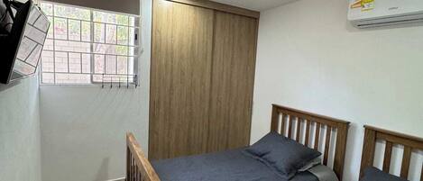 Une petite chambre propre, avec deux lits simples, une fenêtre donnant sur un paysage agréable, un luminaire au plafond et un appareil de climatisation.