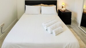 Un letto rifatto con lenzuola bianche e due asciugamani arrotolati, un comodino con una lampada e un condizionatore d'aria a parete.