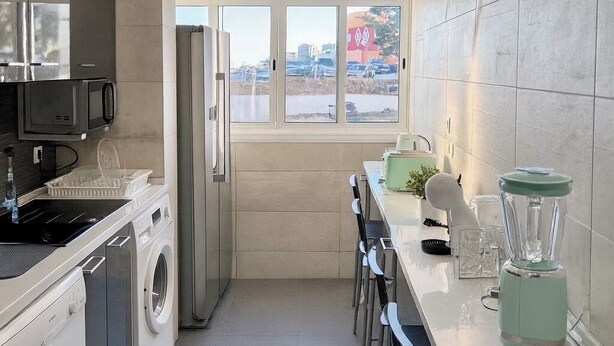 Una cucina moderna con lavatrice, frigorifero, microonde, frullatore e una finestra vista esterna.