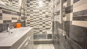 Un bagno moderno con pannelli a mosaico a scacchi, box doccia in vetro e lavabo bianco con dispenser di sapone.