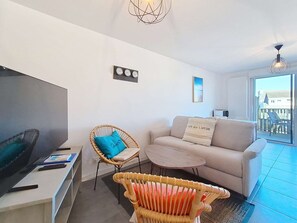 Un salon moderne avec un téléviseur à écran plat, un canapé, un fauteuil en osier et une petite table basse.