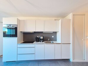 Une cuisine moderne avec des meubles blancs, un four encastré, une machine à café et un évier.