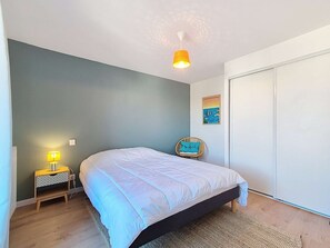 Une chambre à coucher comprenant un lit, une table de chevet, une lampe, une chaise, une armoire et un mur orné d’une affiche.