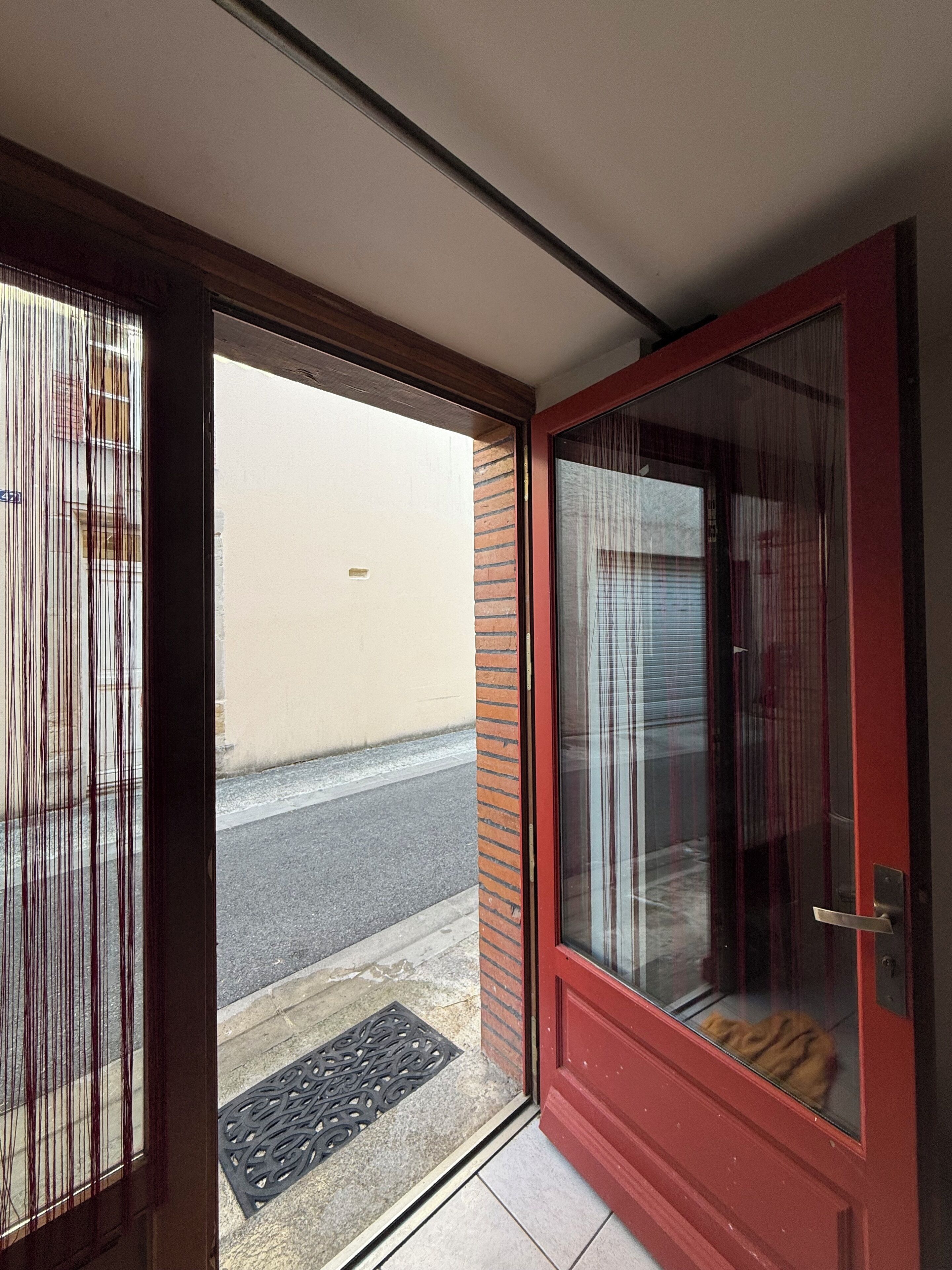 Una porta rossa con un vetrino, un tappetino d'ingresso e vista su una strada e un edificio.