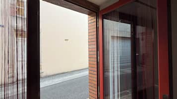 Una porta rossa con un vetrino, un tappetino d'ingresso e vista su una strada e un edificio.