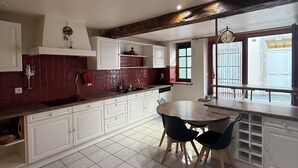 Una cocina con armarios blancos, salpicadero de azulejos rojos, una mesa de comedor de madera con sillas y una ventana con vistas.