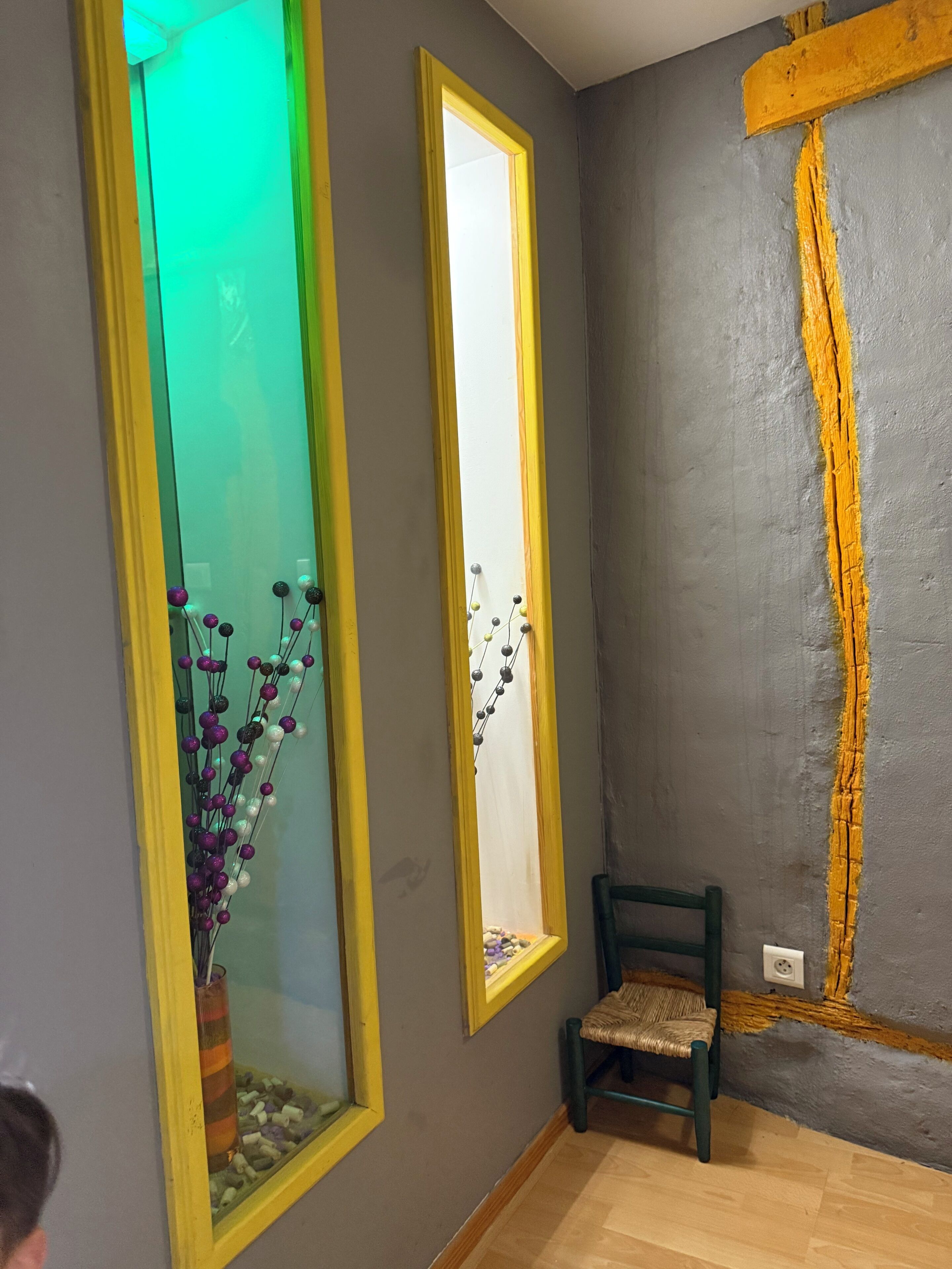 A room with a large mirror, a small chair, and a decorative vase with flowers.