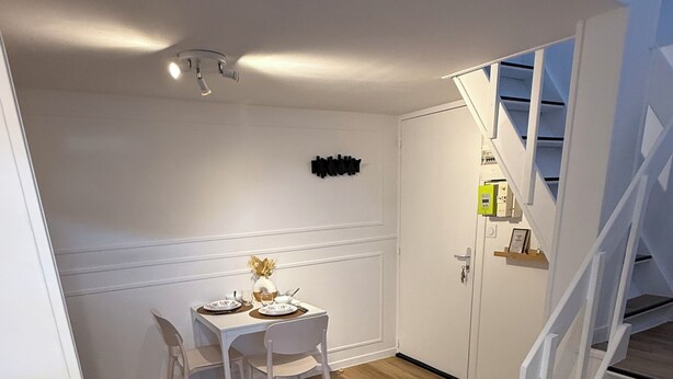 A dining area with a white table set for four, a white chair, a small vase with flowers, and a wall-mounted sign. - The little cocoon (Vierzon)