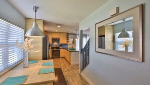 A modern kitchen with wooden cabinets, a dining table with blue placemats, and pendant lighting. - FLIP FLOP LIING 2! 4 Bdrms, 3 Bths, STEPS TO THE SAND! (New Smyrna Beach)