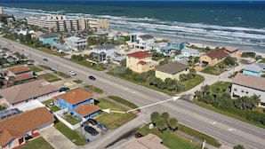 A coastal residential area with a road leading to the beach, houses with various roof colors, and a large building in the background. - FLIP FLOP LIING 2! 4 Bdrms, 3 Bths, STEPS TO THE SAND! (New Smyrna Beach)