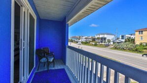 A balcony with a blue wall, a white railing, and a view of a street with houses and cars. - FLIP FLOP LIING 2! 4 Bdrms, 3 Bths, STEPS TO THE SAND! (New Smyrna Beach)