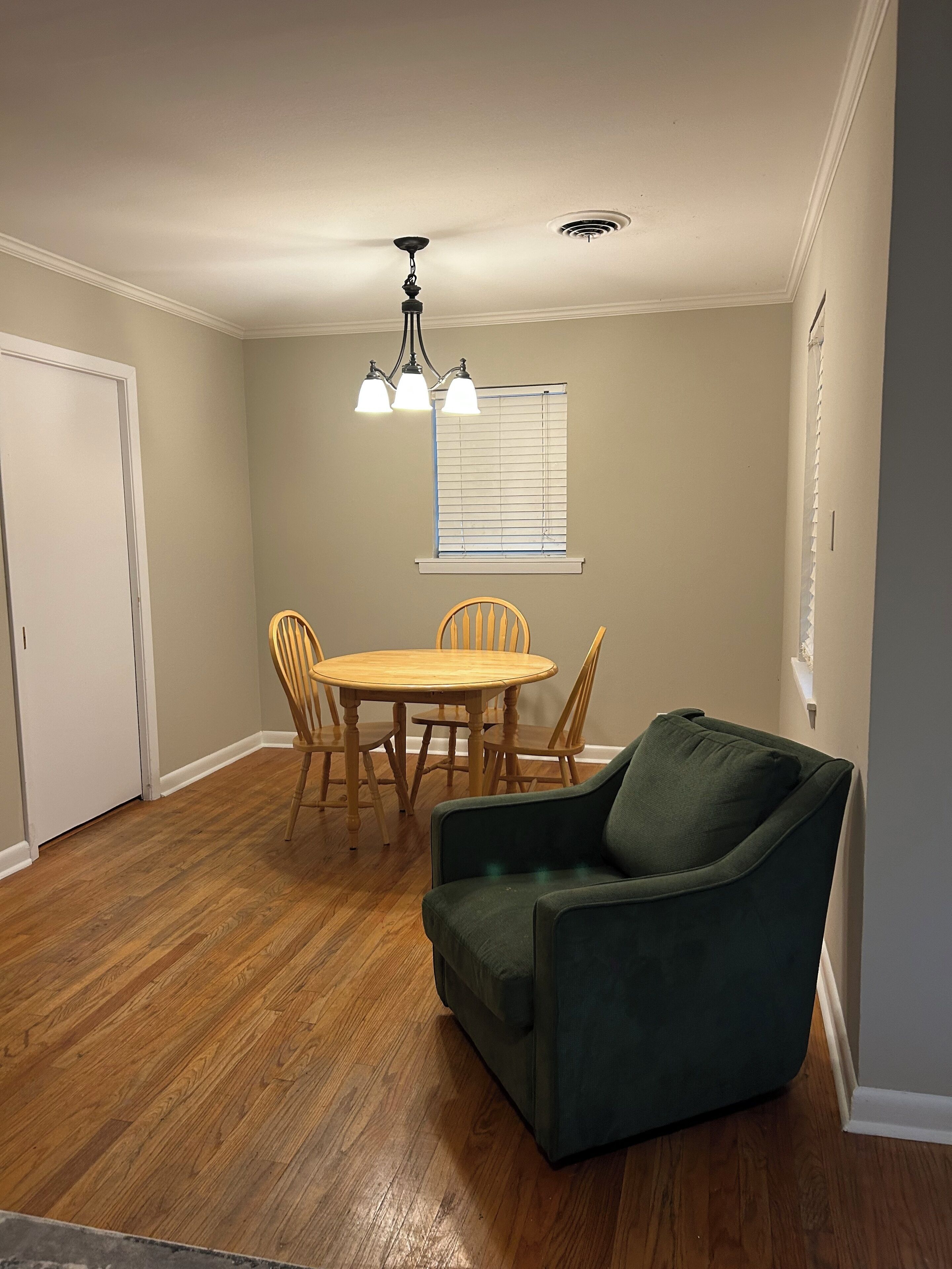 A dining area with a round table and chairs, a green armchair, and a ceiling light fixture.